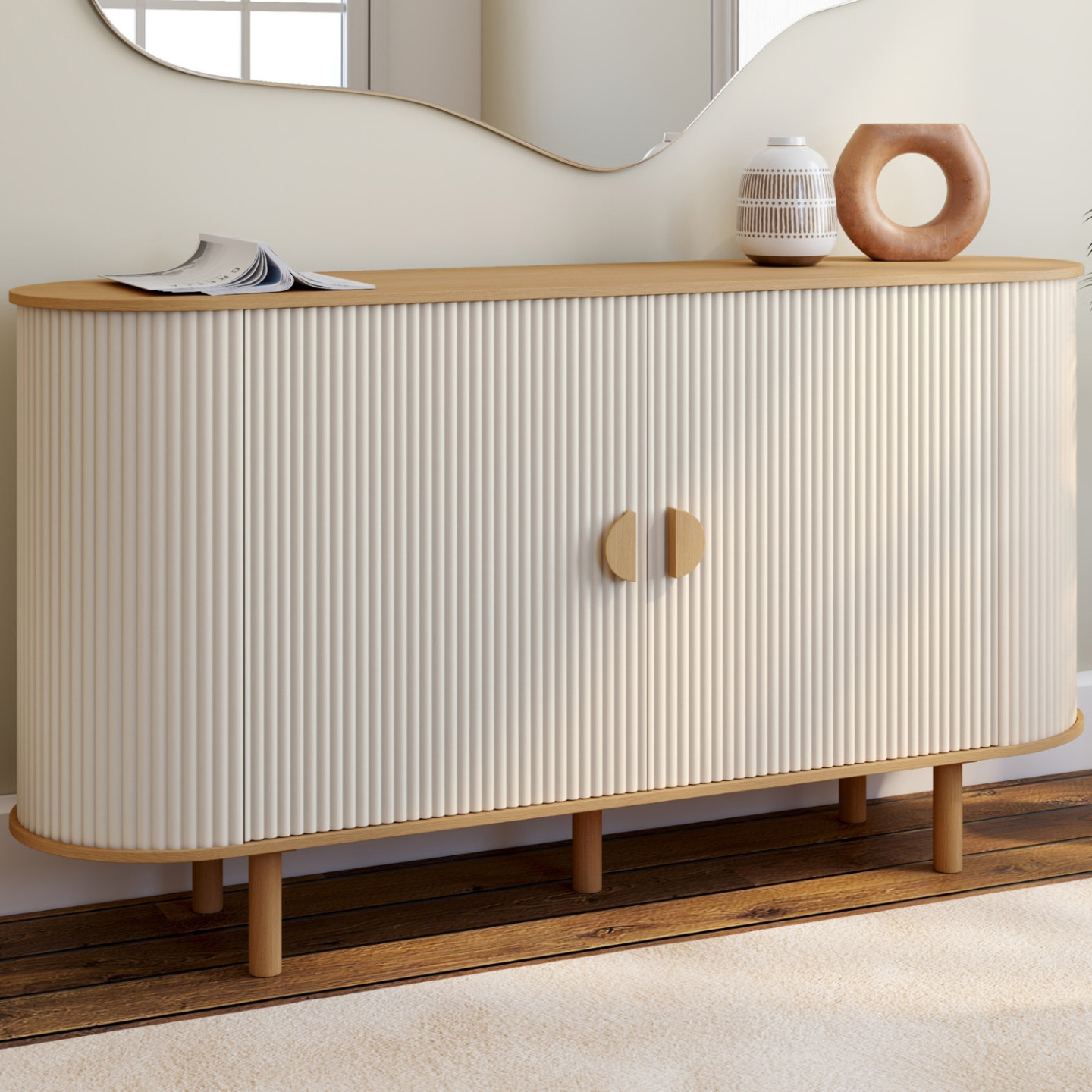 Buffet moderne arrondi aux portes cannelées blanches, plateau en bois clair, dans un salon avec décorations en terre cuite et tableaux abstraits.