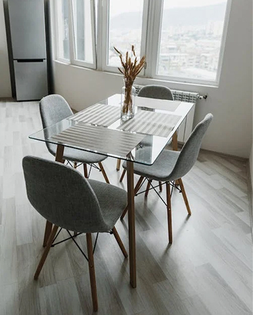 Quatre chaises en tissu gris et pieds en bois autour d’une table en verre
