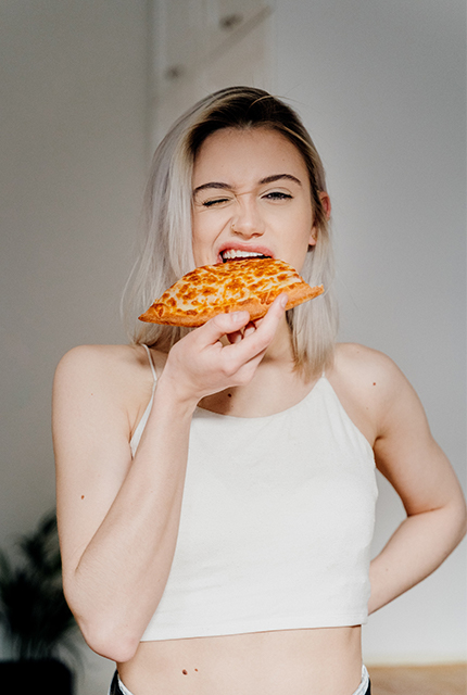 Une femme mangeant une part de pizza debout