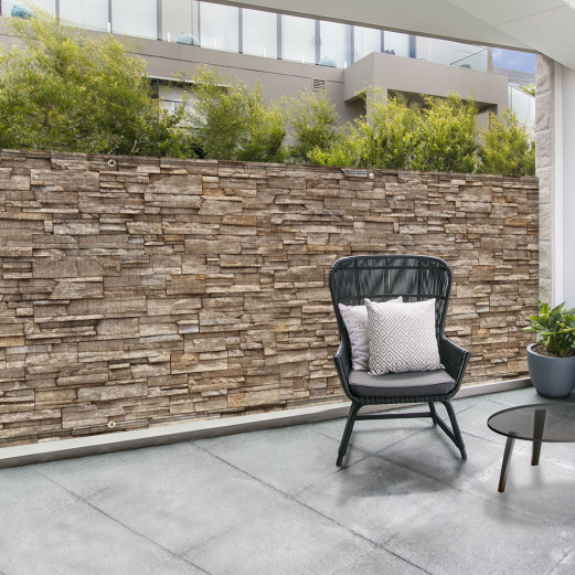 Un brise-vue en toile effet matière mur de pierre protège une terrasse du vis-à-vis