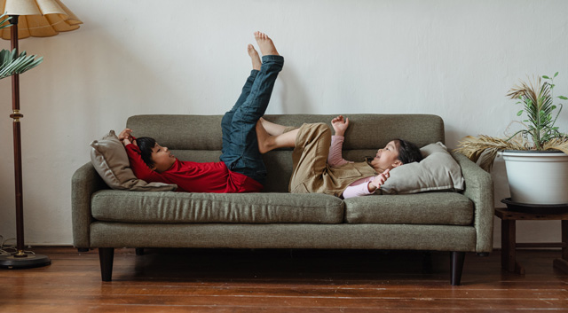 Dans un salon au parquet sombre, deux enfants jouent sur un canapé en tissu gris vert.