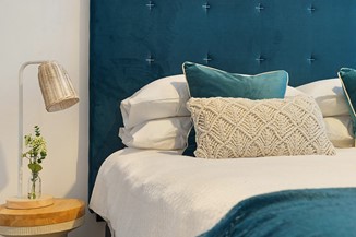 Une tête de lit bleu canard encadre un lit décoré de coussins et d’un plaid