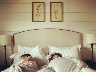 Deux personnes endormies dans un lit moelleux surmonté d’une tête de lit.