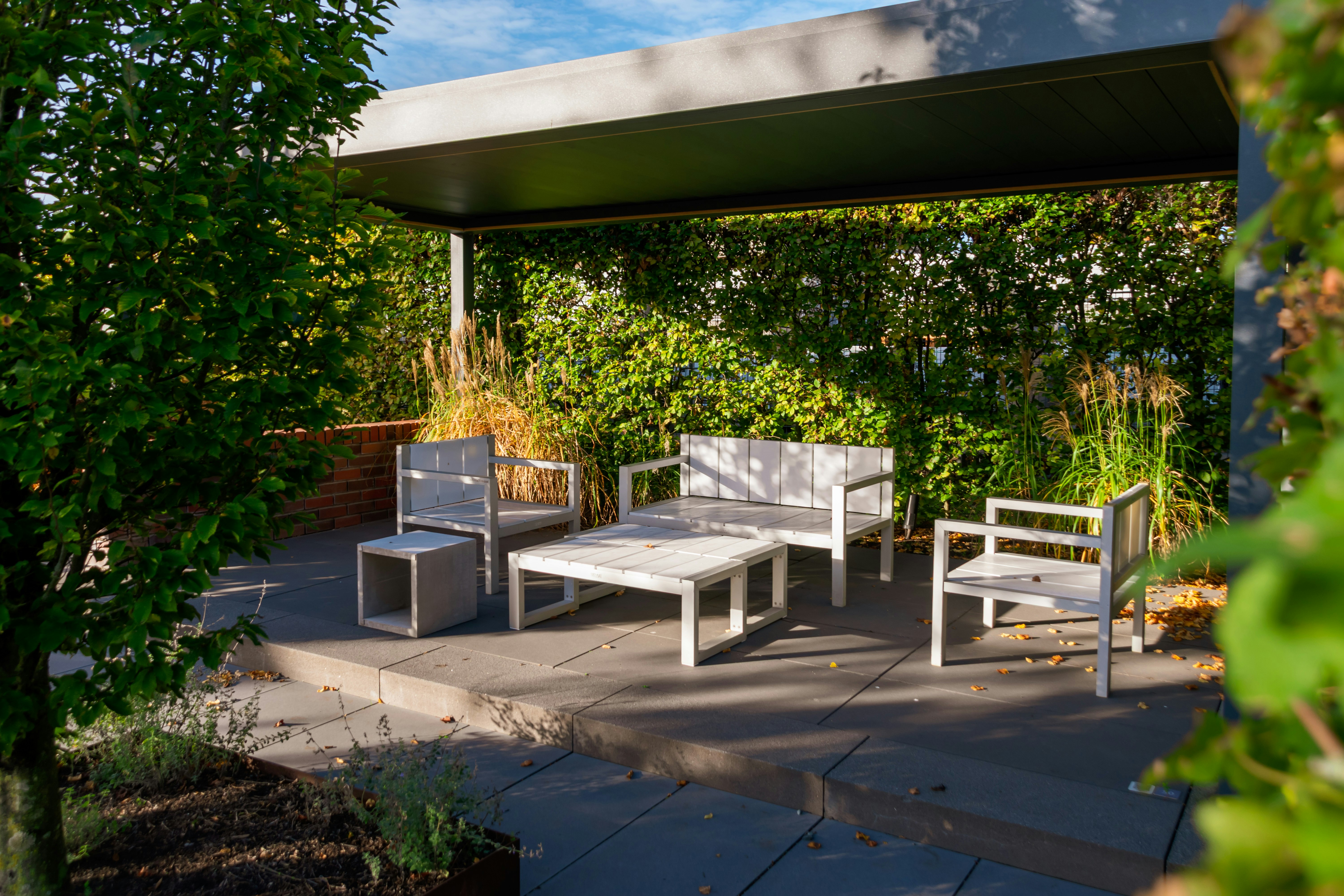 Salon de jardin moderne sur une terrasse aménagée avec des plantes, un tapis extérieur et une tonnelle, idéal pour profiter des beaux jours.
