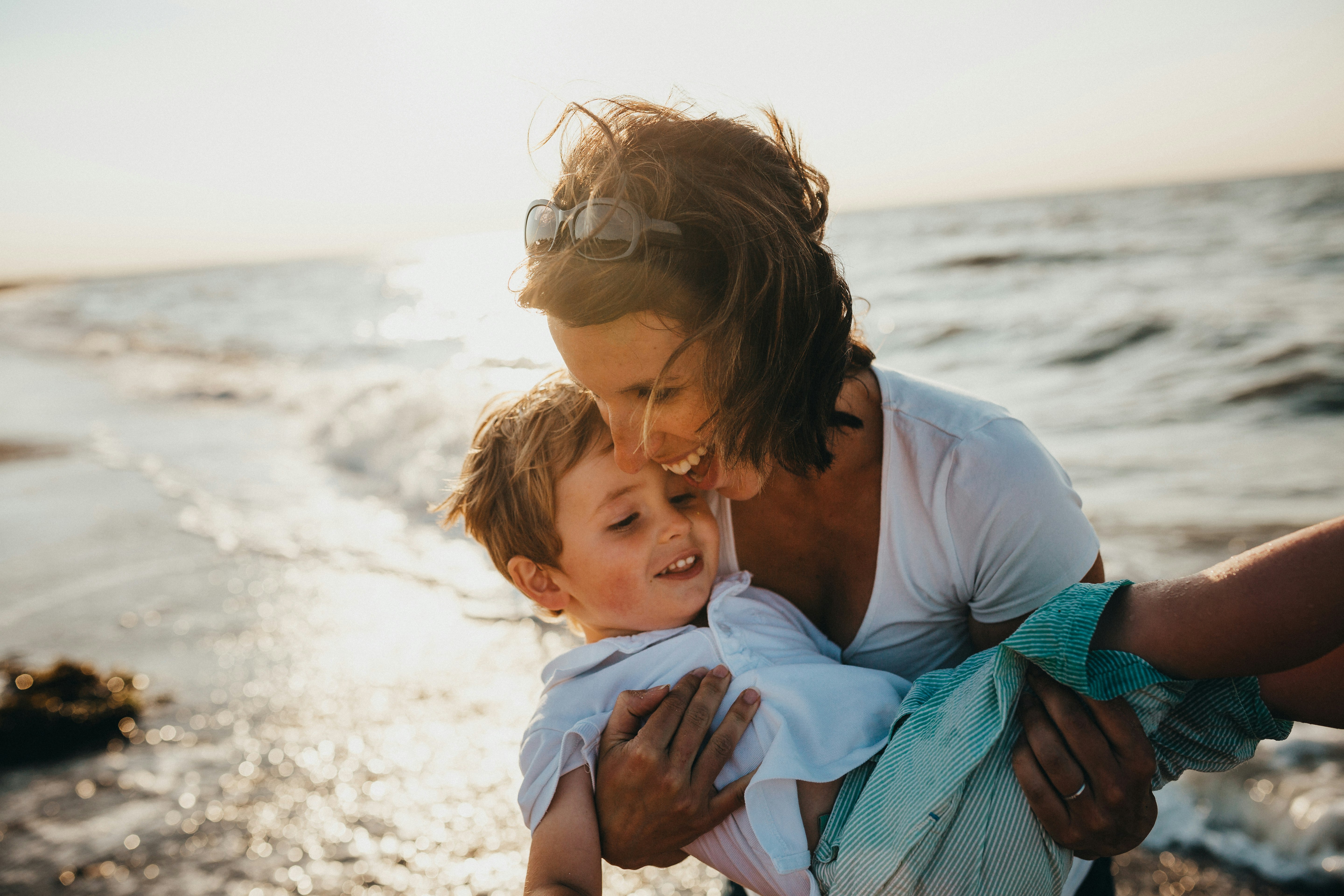 Maman souriante tenant son jeune fils dans ses bras sur une plage au coucher du soleil pour la fête des Mères.