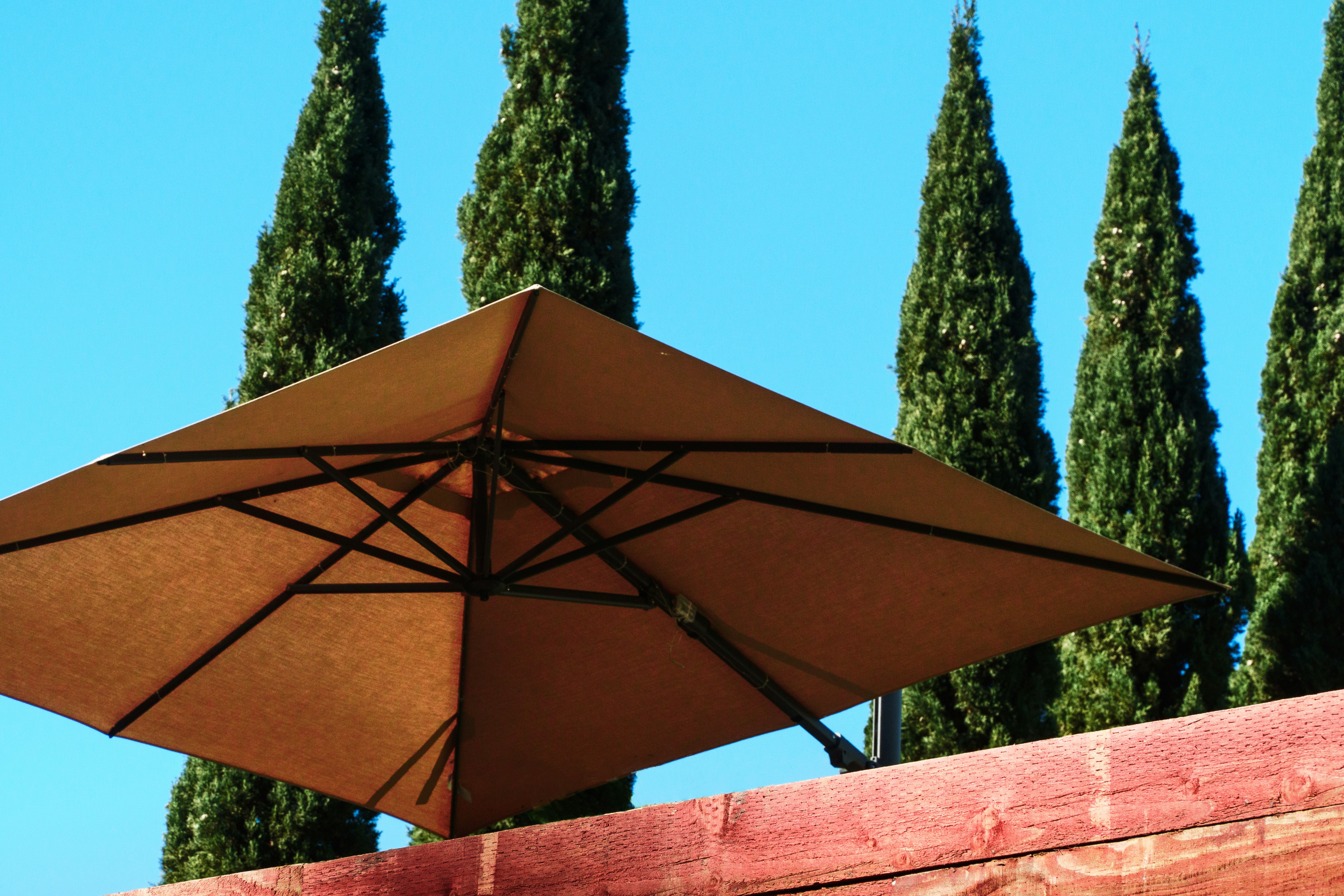 Parasol de jardin beige sur une terrasse avec arbres et ciel bleu en arrière-plan.