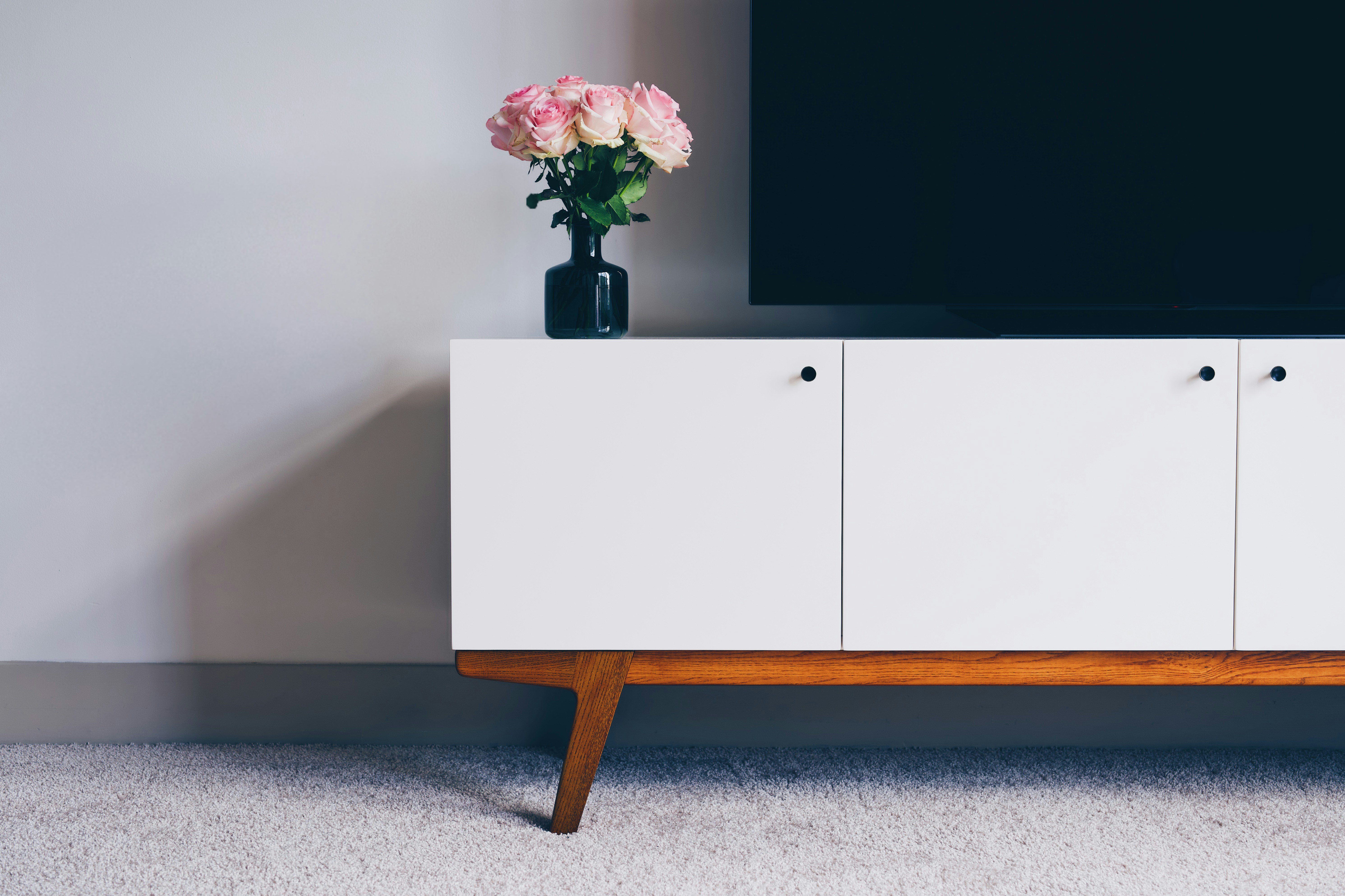 Un meuble TV blanc au design minimaliste avec sur le dessus un écran plat et un vase avec des roses